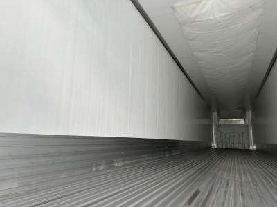 Trailer interior showing long empty refrigerated trailer with ribbed floor and white insulated walls, rear doors visible at far end.