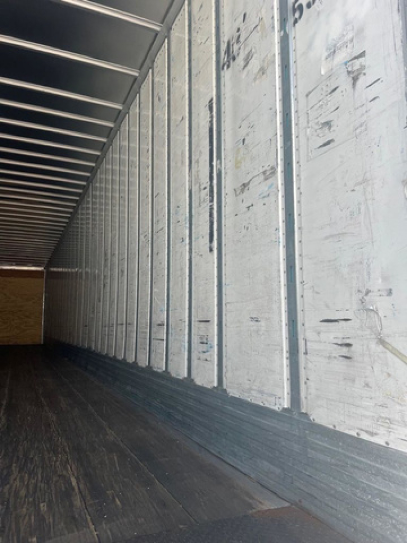 Interior of a cargo trailer showing aluminum side walls with vertical seams and a dark wooden floor.