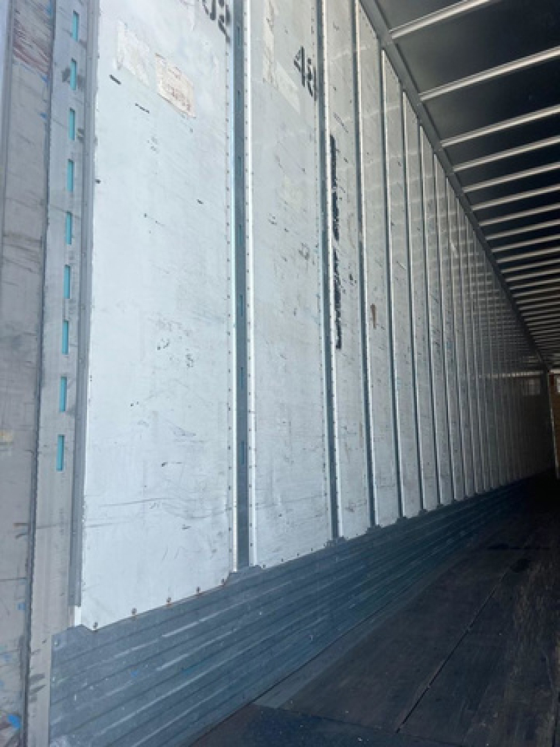 Van trailer interior with metal side walls and ribbed floor, exterior faded light panels along the side.