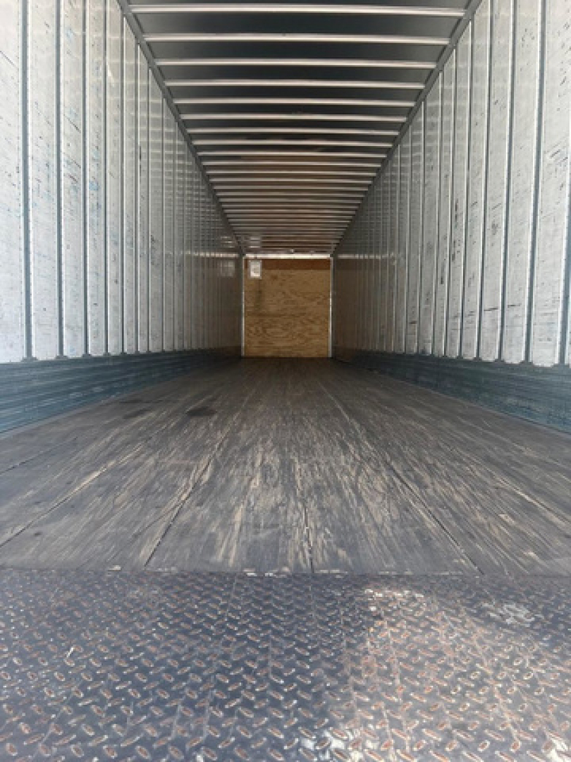 Rear interior of a used utility van trailer showing corrugated metal walls and a wooden bulkhead at far end.