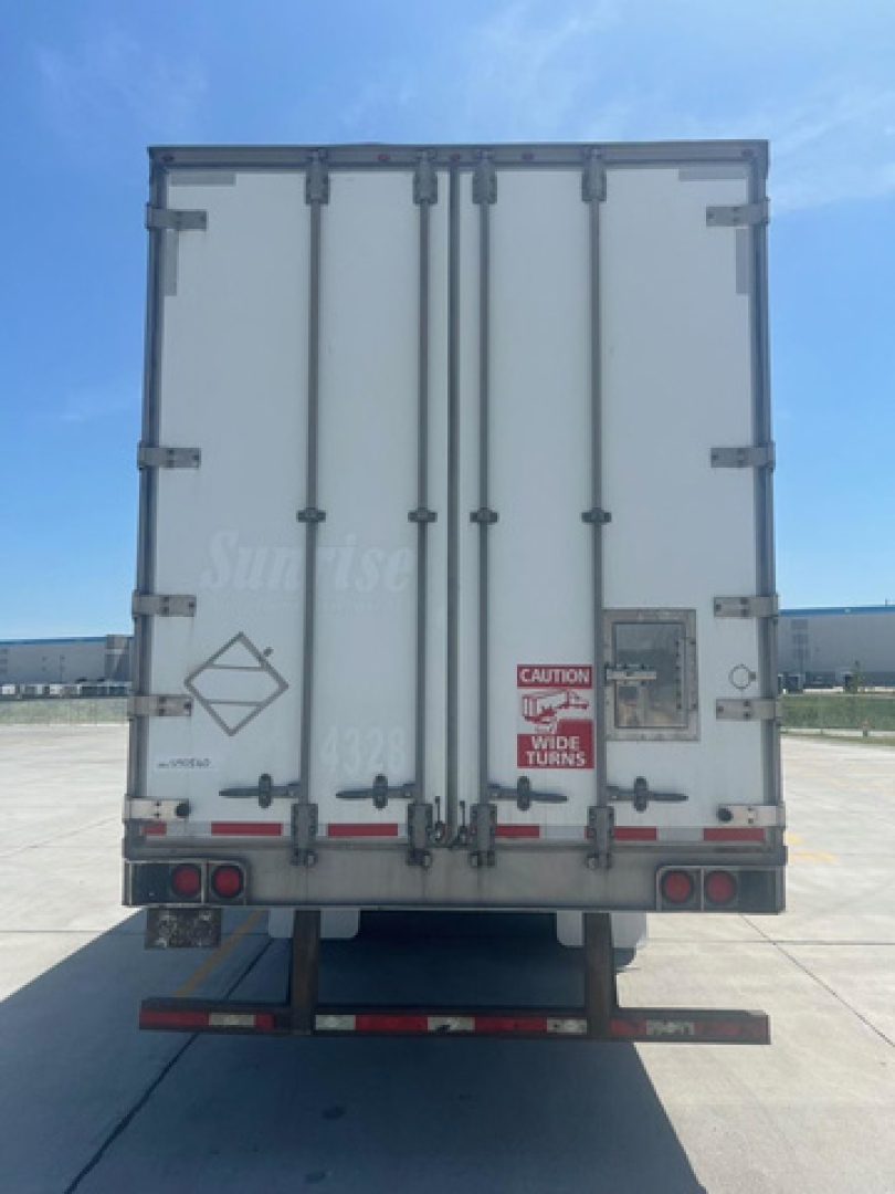 Rear view of a white box trailer with doors closed, warning signage, taillights, and bumper visible.