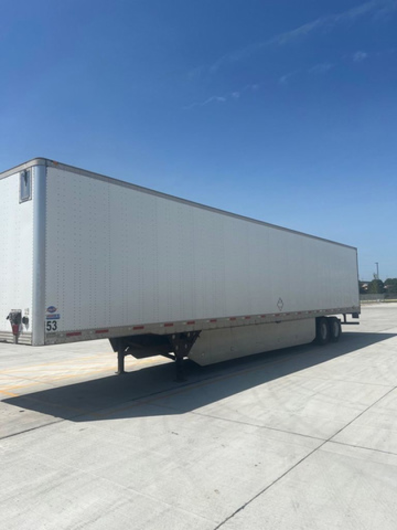 White utility trailer with a boxy rectangular cargo area and tandem axles parked on concrete, side view showing riveted panels.
