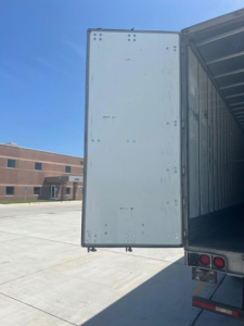 Rear and side of a white box trailer cargo area open at the back with smooth metal doors and riveted panels.