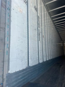 Van trailer interior with metal side walls and ribbed floor, exterior faded light panels along the side.
