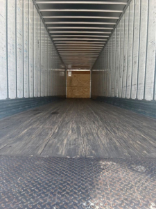 Rear interior of a used utility van trailer showing corrugated metal walls and a wooden bulkhead at far end.