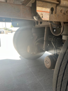 Trailer undercarriage showing wheel hub and suspension with warning label and frame components visible.