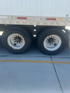 Two trailer tires on a utility van side view with wheel rims and a portion of the cargo body above; no legible model text visible on image.