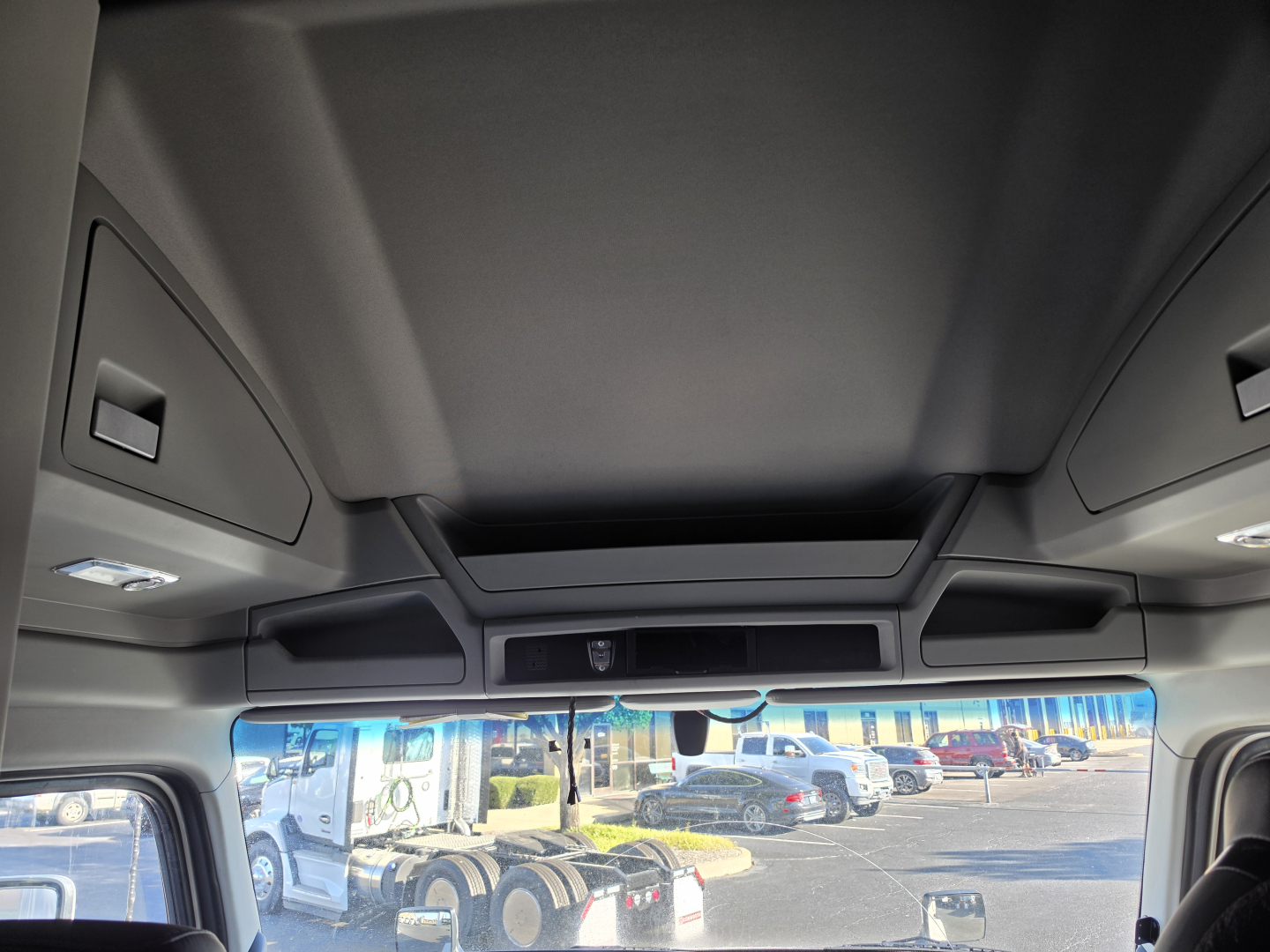 Kenworth T680 cab interior view showing overhead storage compartments and windshield with reflection of lot; no obvious labels visible.