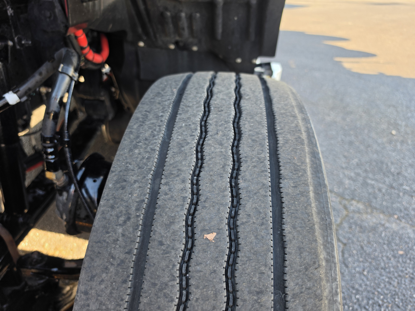 Kenworth T680 truck undercarriage showing front dual rear axle area and stacked tires. Visible details include wiring and hydraulic lines near the chassis.