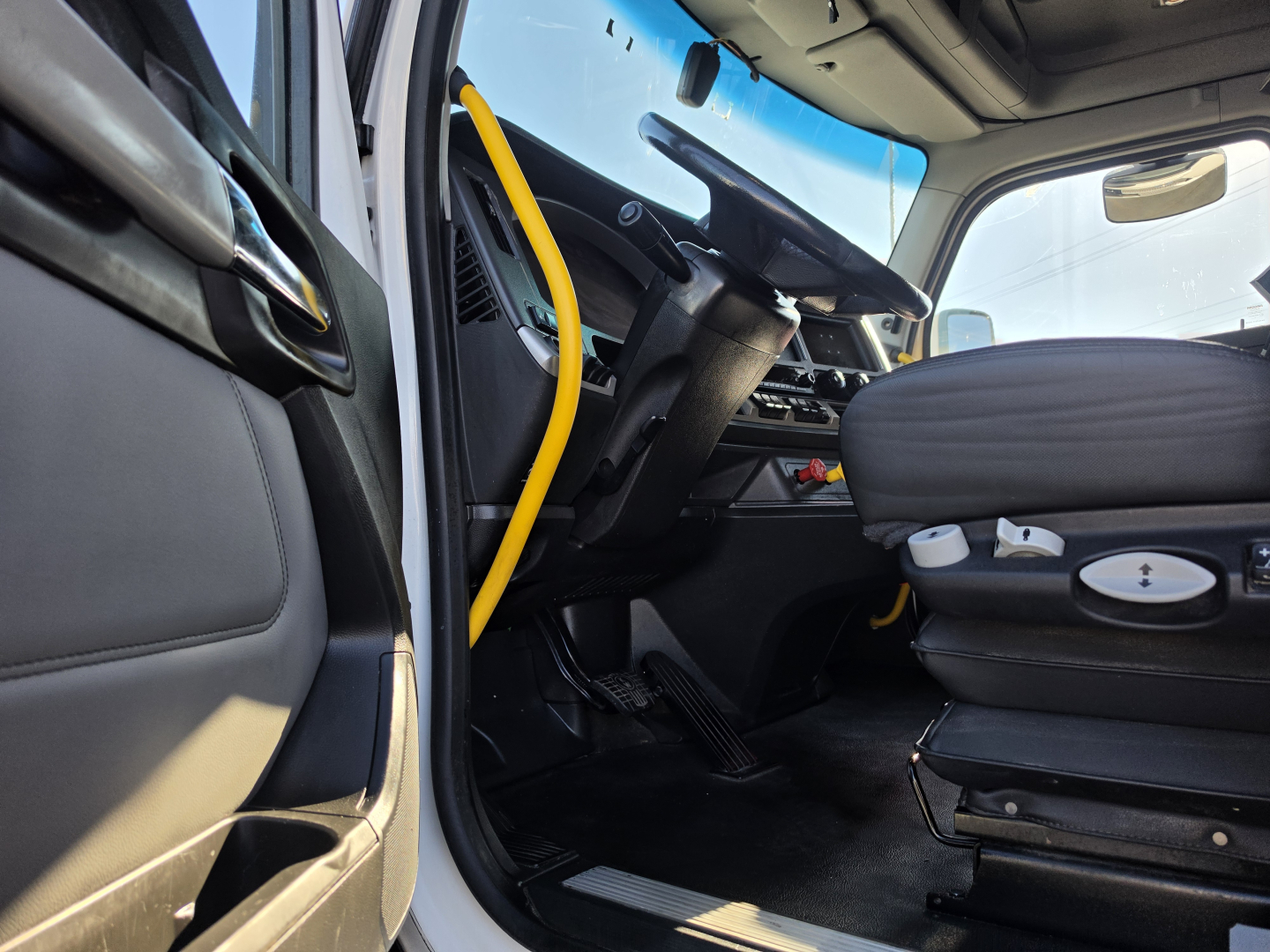 Interior of a 2023 Kenworth T680 truck cab, driver seat and steering wheel visible from open door, with yellow handrail and dashboard controls.