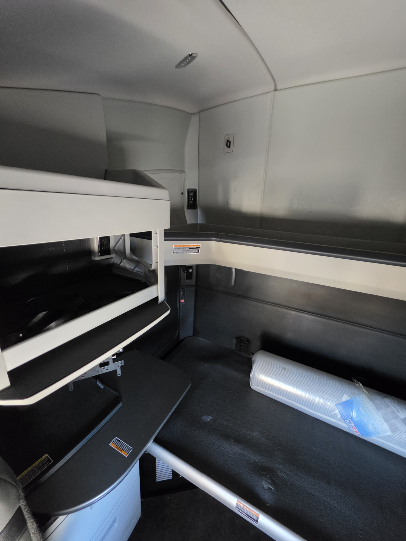 Kenworth T680 cab interior showing sleeper bunk area with storage compartments and a plastic water bottle on the floor.