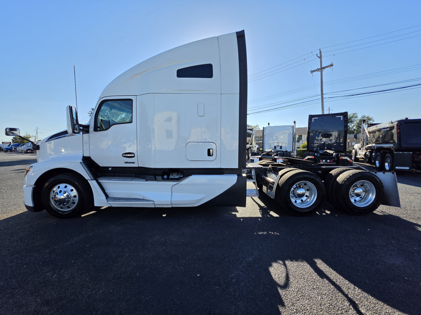 Kenworth T680 side view cab and frame showing 2023 model, white exterior, fuel tanks, and tandem rear axles.