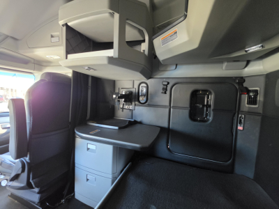 Kenworth T680 cab interior showing sleeper area with overhead storage, side panel with compartments, and desk/drawer unit.