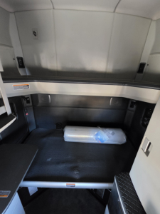 Kenworth T680 cab interior cargo area view with sleeping area and storage shelf, blank walls, and a small packaged item on the floor.