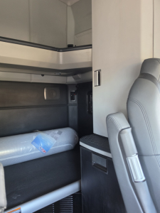 Kenworth truck cab interior showing sleeper berth area with a mattress in plastic, side panel, and storage compartments.