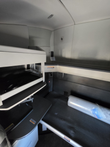 Kenworth T680 cab interior showing sleeper bunk area with storage compartments and a plastic water bottle on the floor.