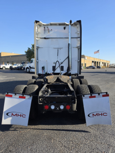 Truck rear view of a used 2023 Kenworth T680 with fifth-wheel area and mud flaps showing MHC branding, rear lights, and truck chassis.