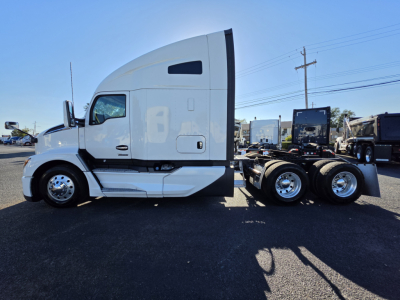 Kenworth T680 side view cab and frame showing 2023 model, white exterior, fuel tanks, and tandem rear axles.