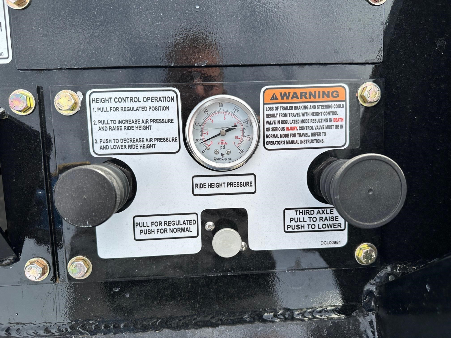 Lowboy trailer front control panel showing height control operation labels, gauge, and knobs; warning and operation stickers labeled ‘Height Control Operation’ and ‘Third Axle’ with dial in center.