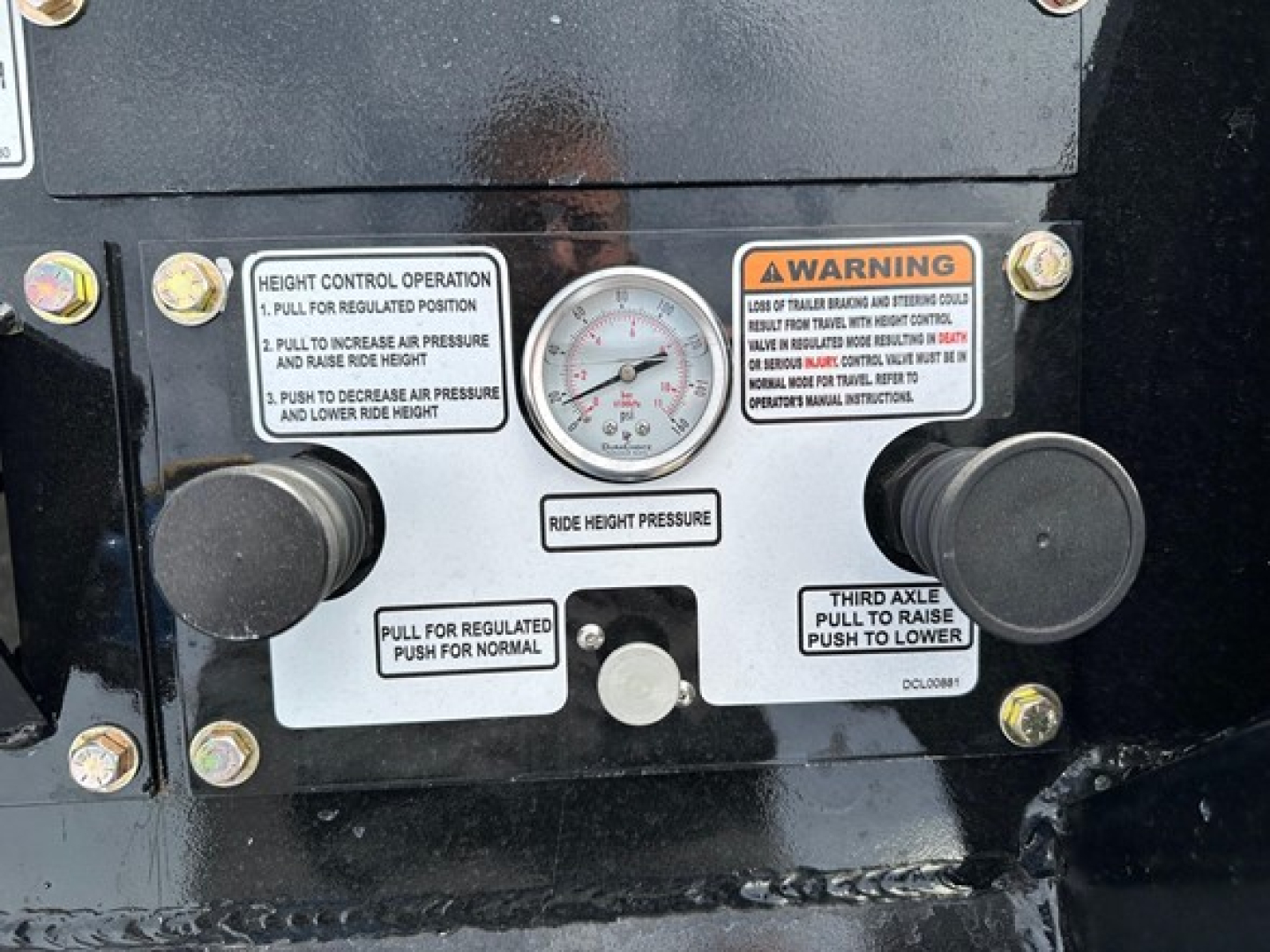 Lowboy trailer control panel with height gauge, warning labels, and two large black knobs; visible text includes height control operation steps and third axle label.