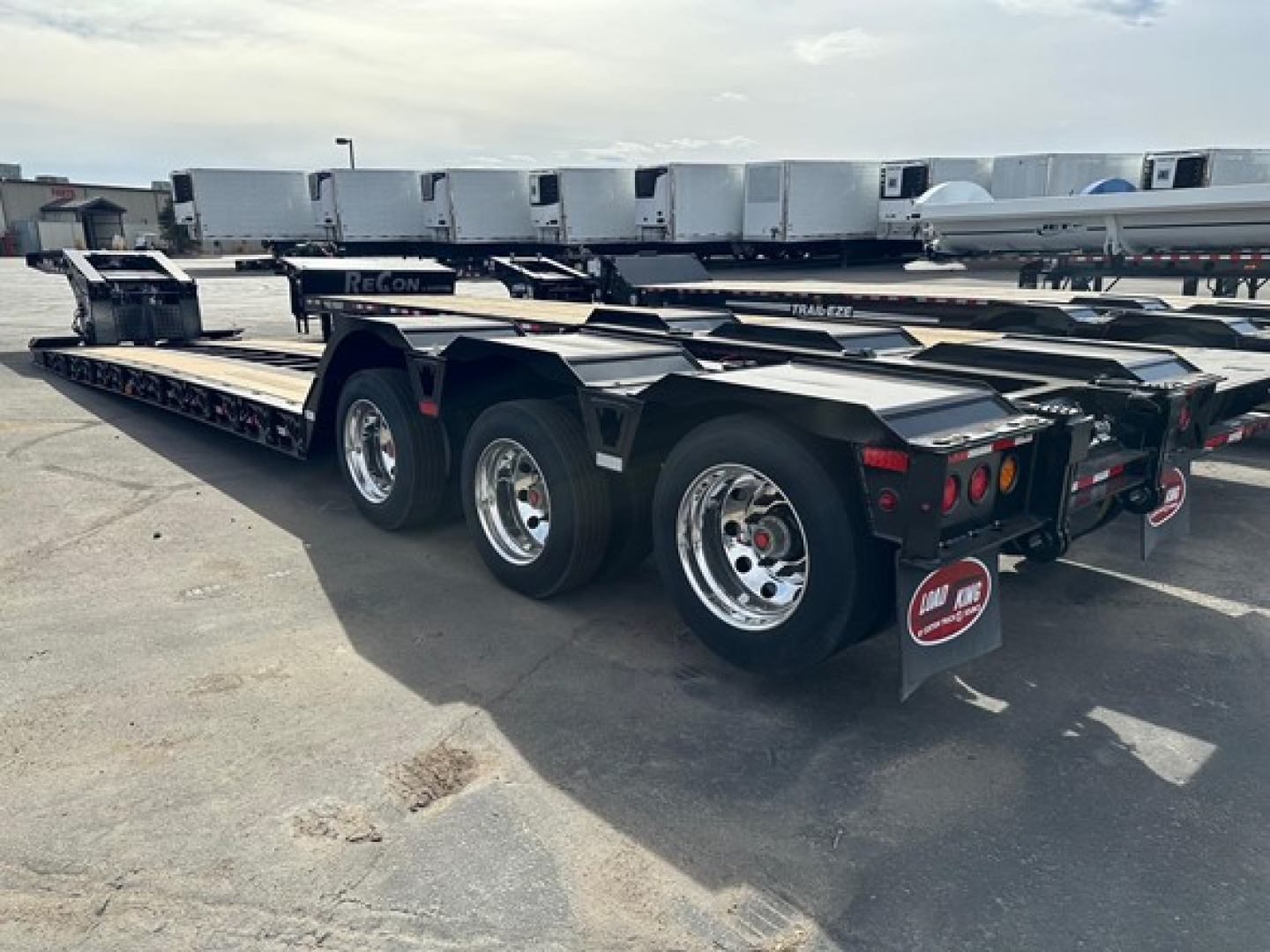 Load King lowboy trailer with multiple axles and polished wheels, showing rear and side profile with reflective black frame and trailer parts.