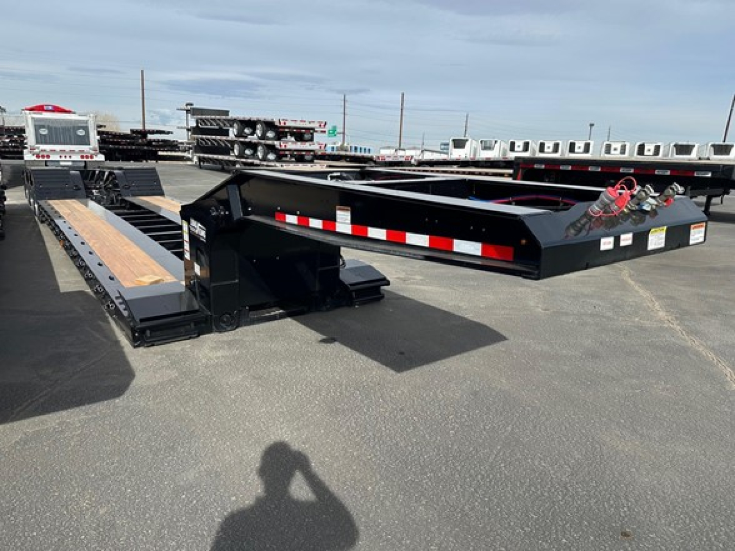 Lowboy trailer by Load King with black frame and wooden deck, side rails, and red-and-white reflective tape; flatbed style with gooseneck/transition sections visible.