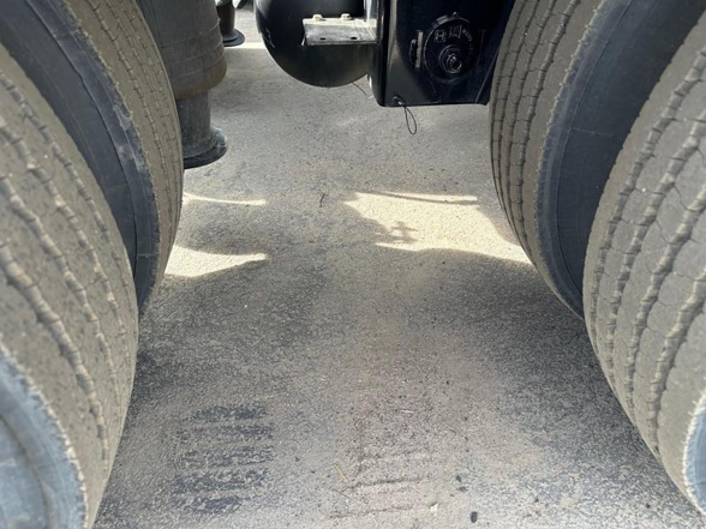 Lowboy trailer chassis between dual rear axles showing landing gear mount and suspension area with dirt on the ground.