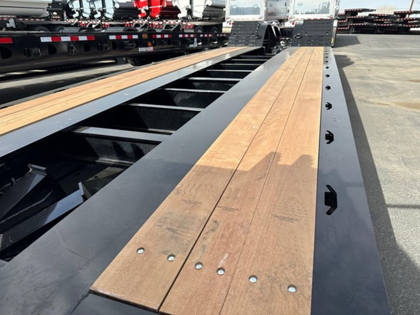 Lowboy trailer deck with wooden planks and steel girders, viewed from close along the bed showing surface screws and side rails.