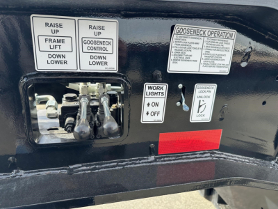 Control panel on a Load King 55 Ton lowboy trailer showing levers and stickers. Visible text includes phrases: 'RAISE UP', 'FRAME LIFT', 'GOOSENECK CONTROL', 'WORK LIGHTS ON OFF', 'GOOSENECK OPERATION' and a long instructional label. The VI