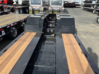 Lowboy trailer deck of a 2027 Load King 55 Ton showing wooden floor panels and hydraulic components in center, front view with neighboring trailers.