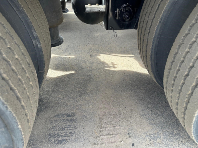 Lowboy trailer view between dual rear axles showing asphalt surface and suspension components.