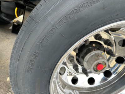Lowboy trailer wheel and tire close-up showing stamped lettering on tire sidewall.