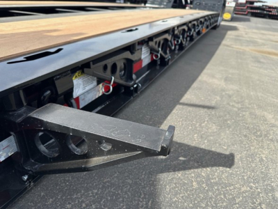 Lowboy trailer with wooden deck and side rails showing a load extension/kingpin area and hydraulic components along the frame.