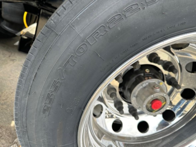 Load King lowboy trailer wheel close-up showing tire and chrome rim with printed tire model text visible.