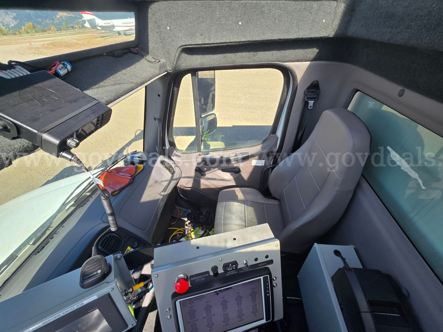 Cab interior of a Freightliner truck showing dashboard panel with electronic control screen, steering wheel, seat, door, and window; equipment and wiring visible.