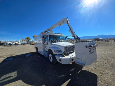 Truck with mounted boom crane and front bucket in an open lot, 2023 Freightliner 2200SEB utility body showing crane arm and bucket on the passenger side.