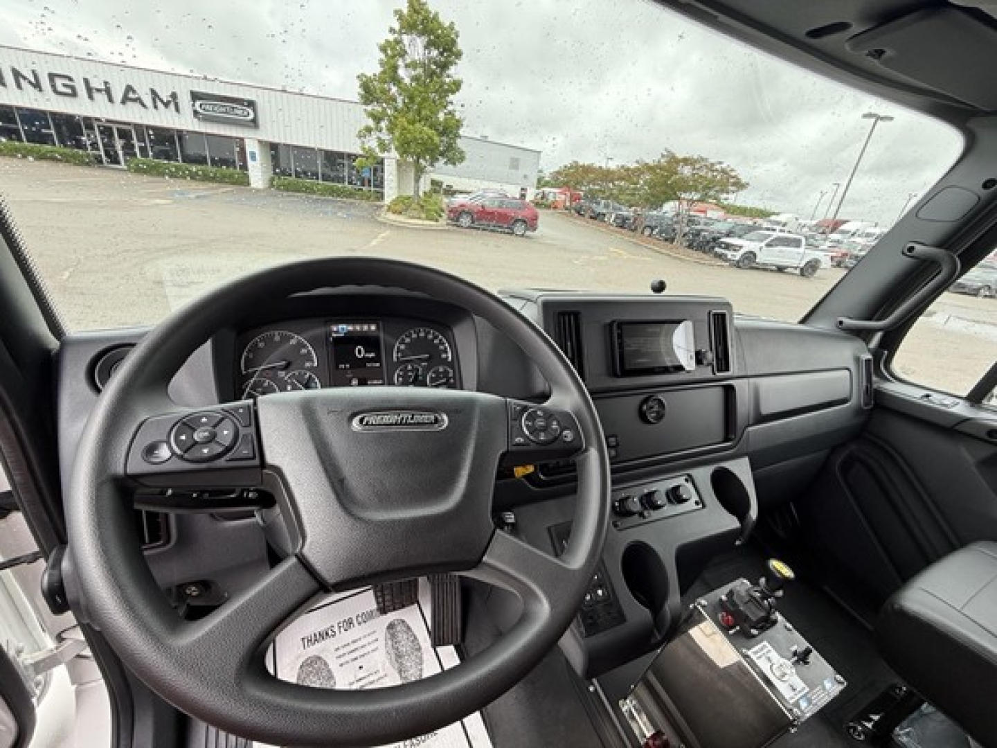 Dashboard and steering wheel view inside Freightliner M2 106 cab showing instrument cluster and center console with digital display.