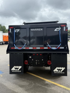 Dump truck dump bed with 'WARREN' branding on the back, blue straps hanging, red taillights, mudflaps with Warren logo.