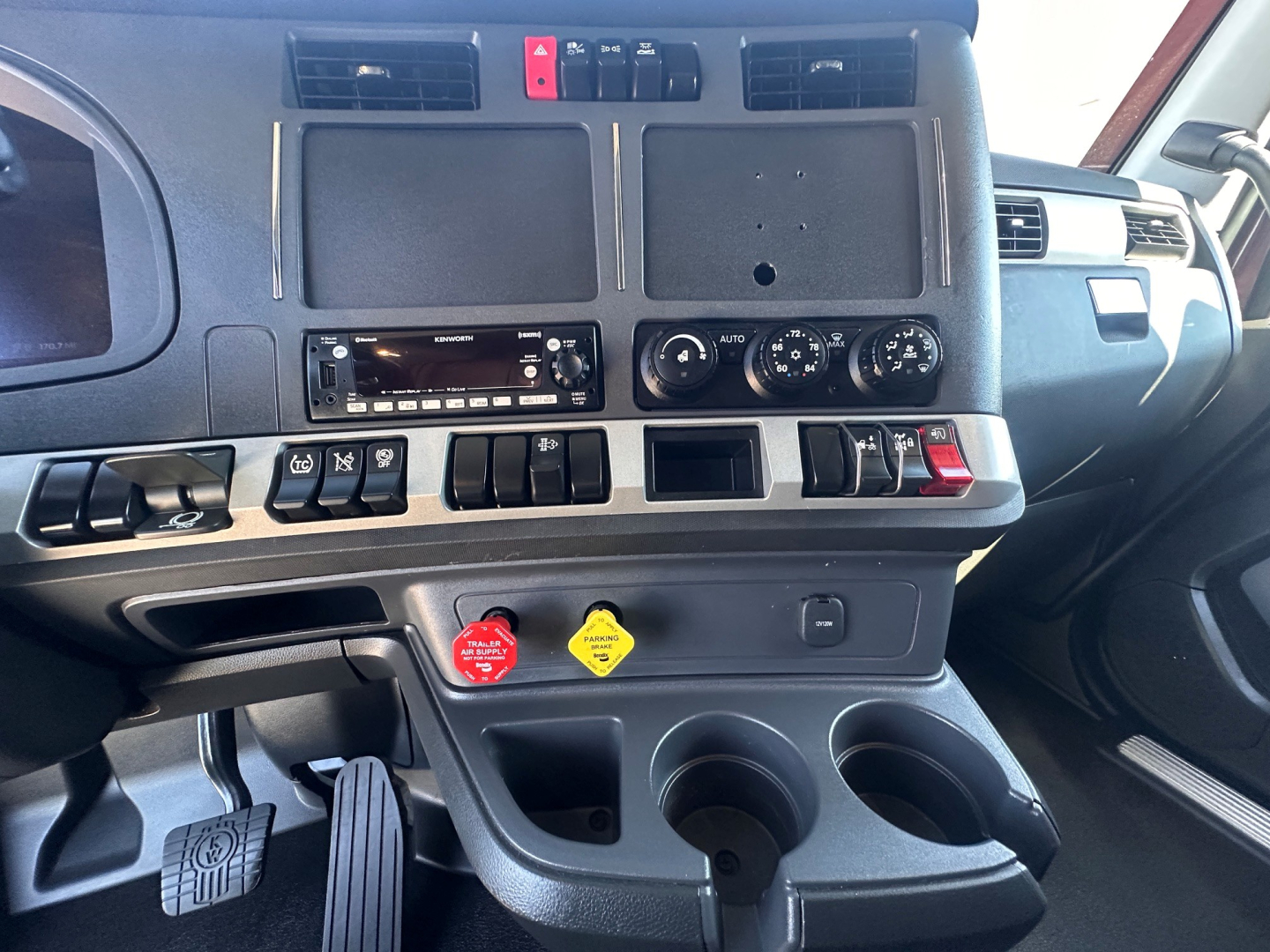 Cab interior of a Kenworth T680 showing dashboard controls, dual cup holders, and a red hazard lever; VIN and stock number not visible in the image.