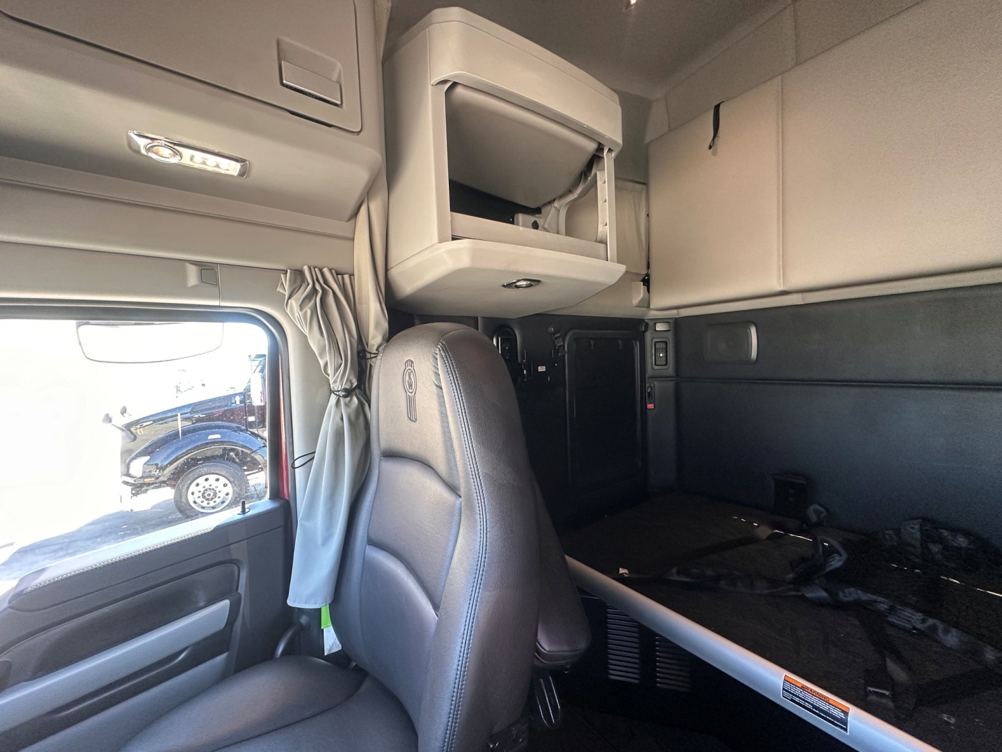 Kenworth T680 cab interior showing sleeper area, dashboard window, and mounted overhead storage cabinet.