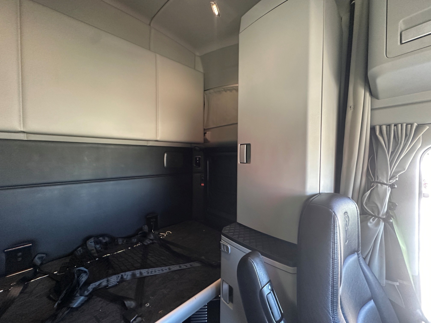 Kenworth T680 cab interior showing sleeper area and partition with storage cabinets and seat visible.