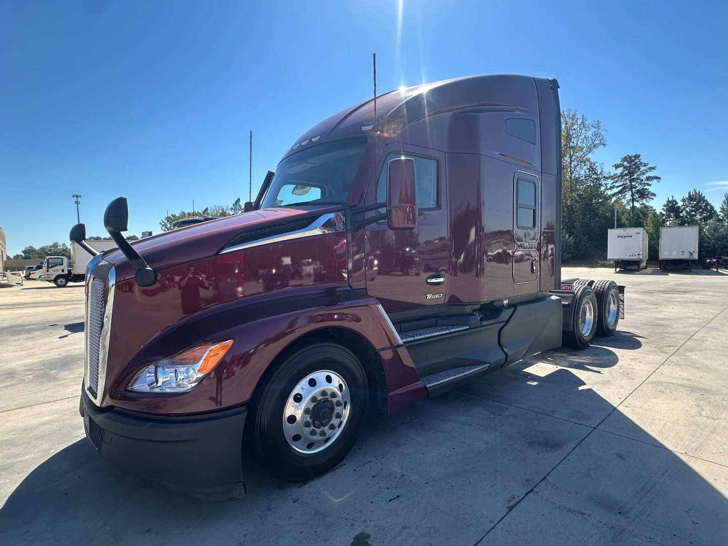 Kenworth T680 6x4 sleeper cab tractor in maroon with chrome wheels, side mirrors, and aerodynamic hood viewed from front-left.