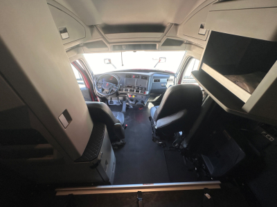 Kenworth T680 cab interior showing driver and passenger seats, dashboard, and overhead storage with a widescreen display.