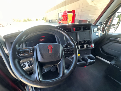 Cab interior of 2023 Kenworth T680 showing steering wheel, dashboard, steering column controls, and center console with cup holders.