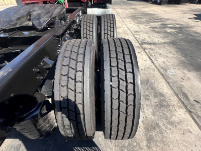 Kenworth T680 rear dual tires with tread and suspension components visible in a truck yard, close-up view of wheel assemblies.