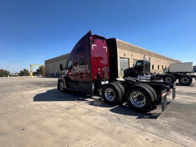Kenworth T680 tractor-trailer cab and rear axles viewed from left side in a parking lot with a blue sky.