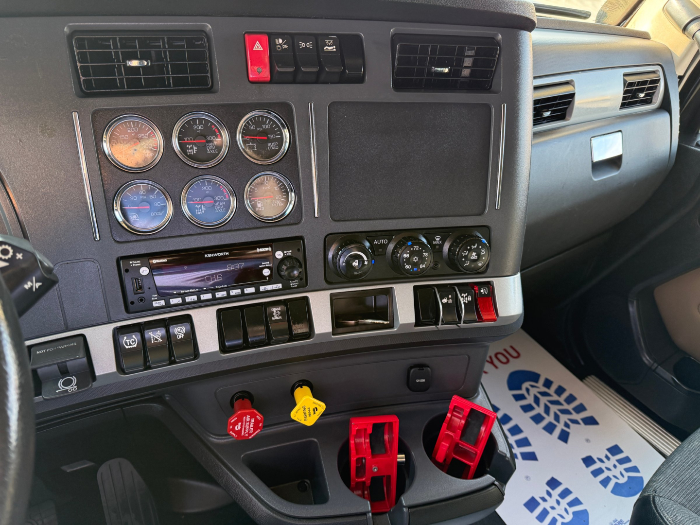 Kenworth T680 dashboard center panel with multiple gauges, switches, and red emergency handles visible.