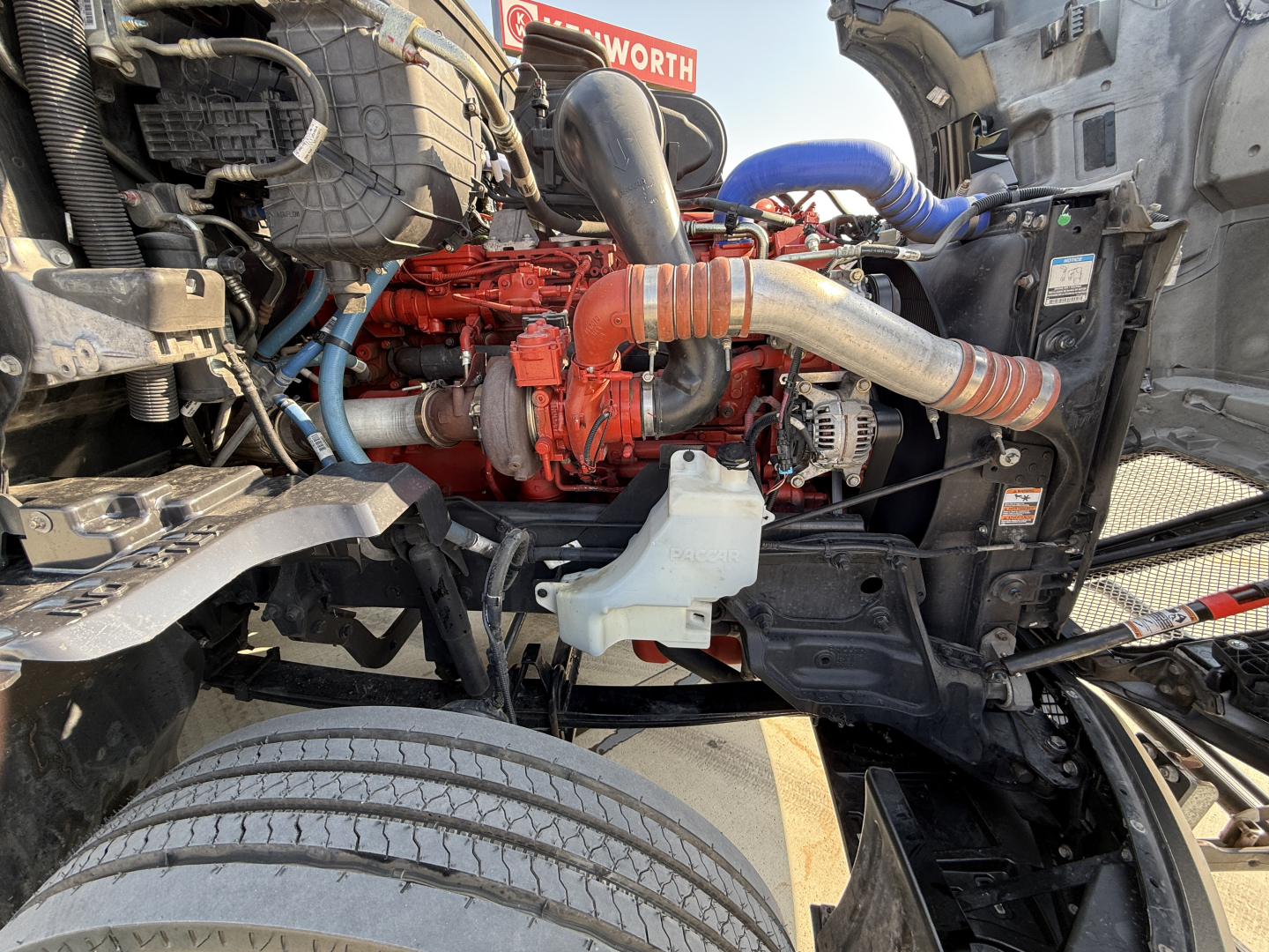 Kenworth T680 engine bay showing diesel engine with red block, intake piping, hoses, and radiator area visible.