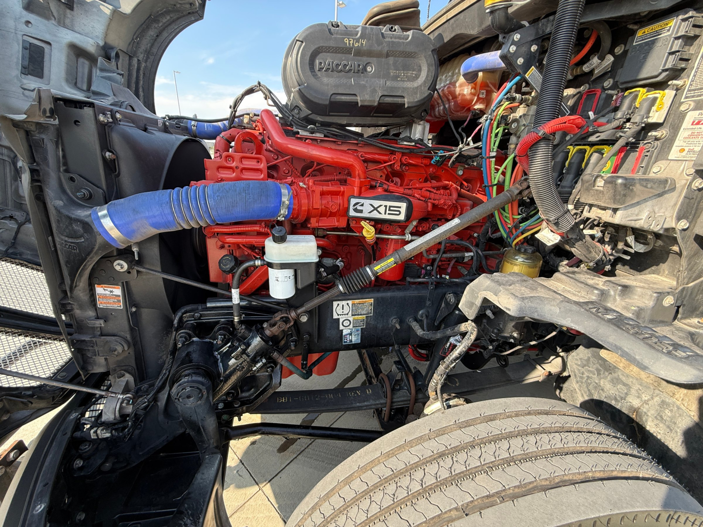Kenworth T680 engine bay showing red Cummins X15 engine and surrounding wiring and hoses.