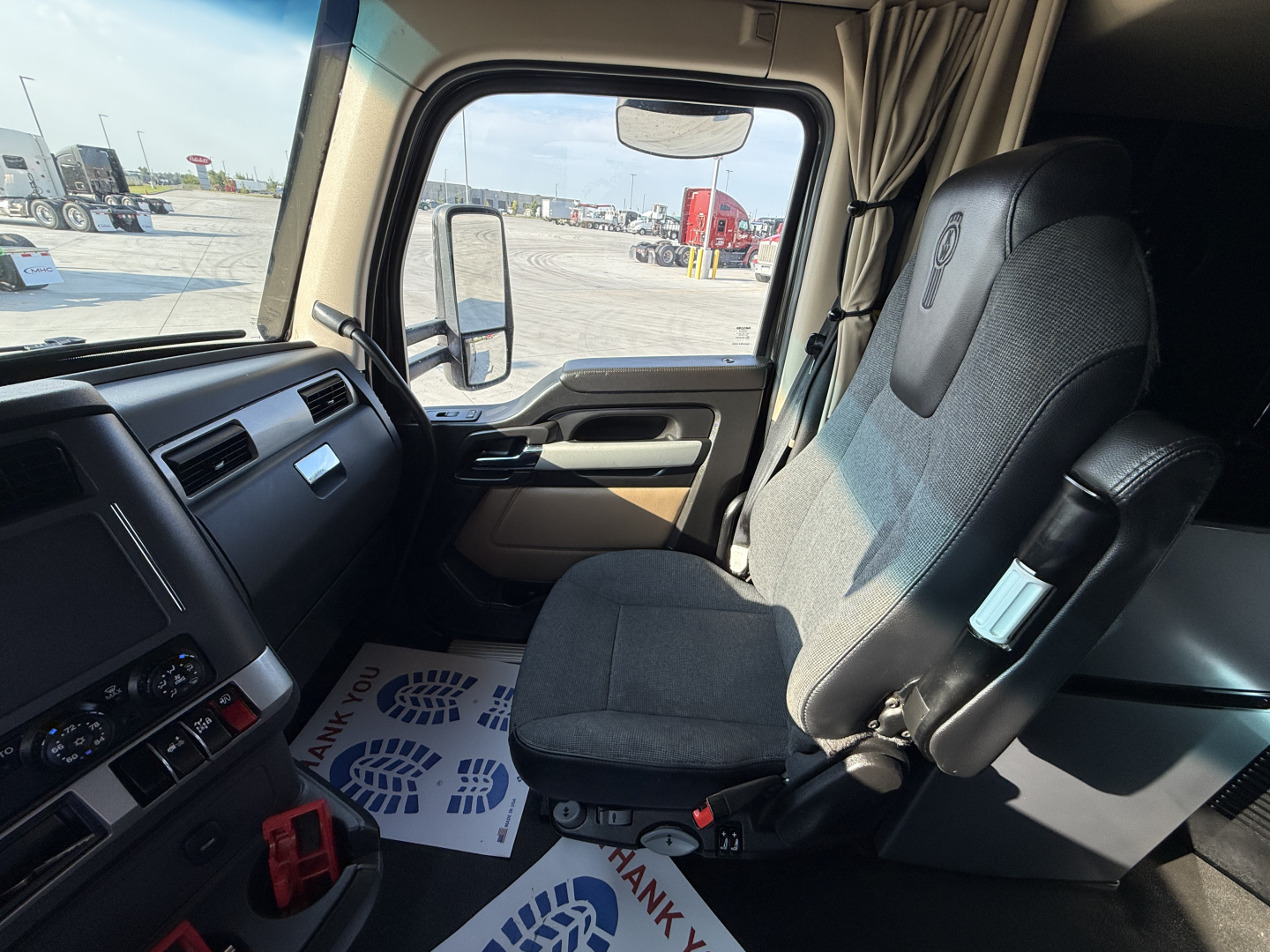 Kenworth T680 truck interior dashboard and passenger seat view from driver side showing steering wheel, dashboard controls, and window.